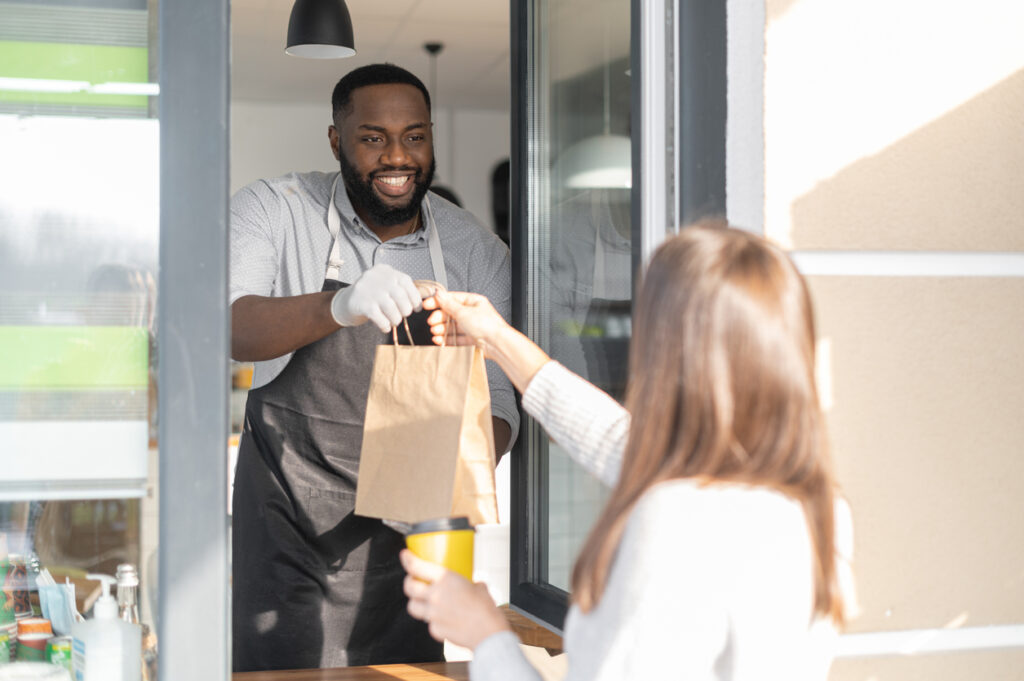 A friendly and smiling franchise owner is serving a female customer take-out order through window